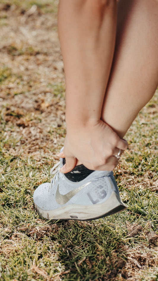 Person holding the foot and ankle area while wearing a running shoe outdoors