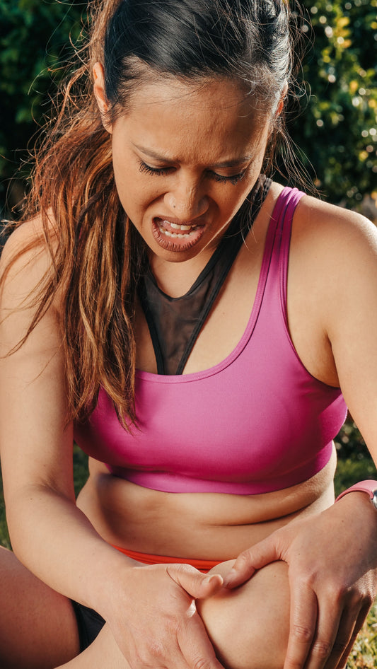 Woman in sports clothing holding her knee while seated outdoors