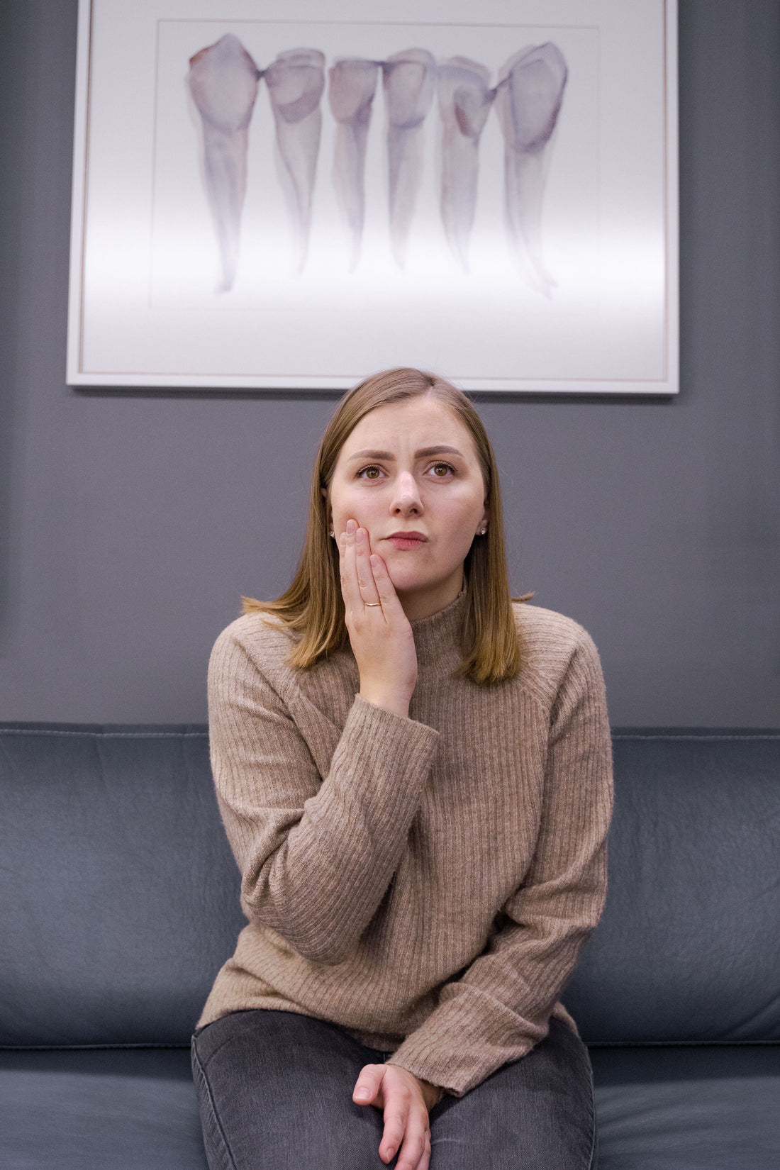 Woman holding her cheek while experiencing facial and jaw pain in a dental clinic
